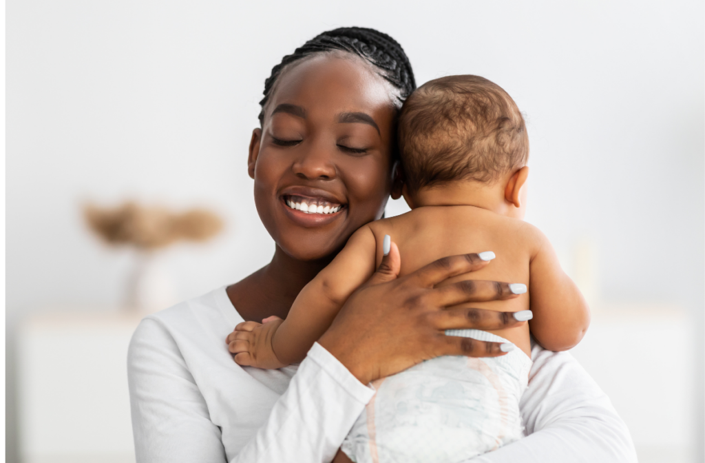 Black woman who is a nanny or postpartum doula holding and hugging a newborn baby.